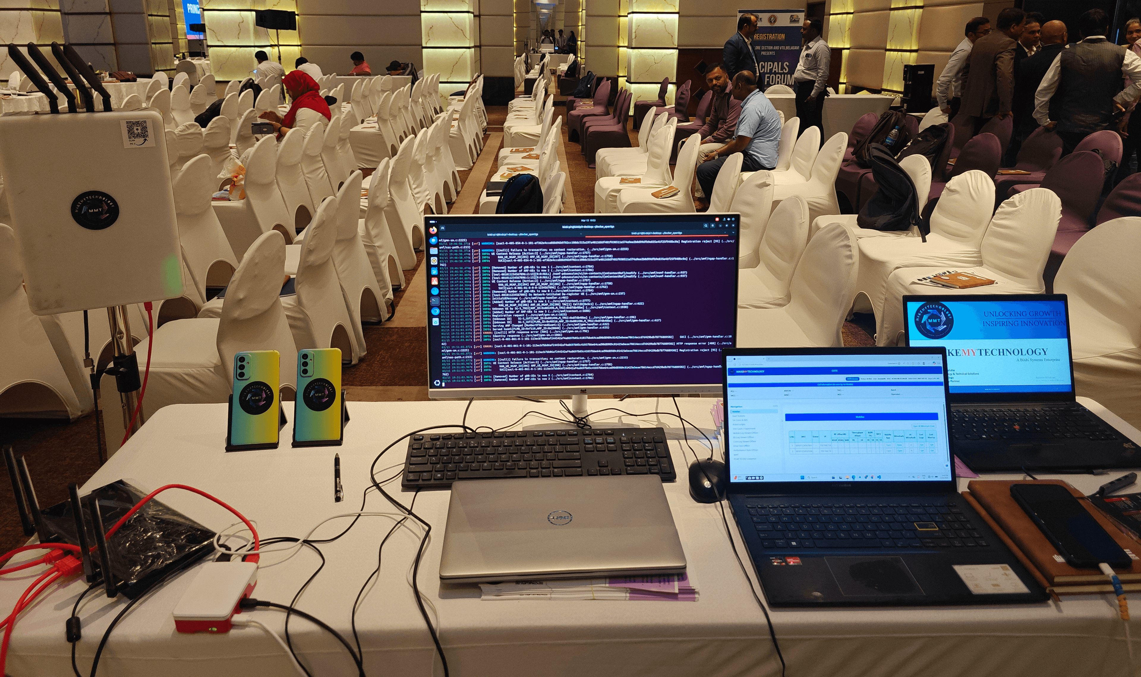MMT 5G/6G Studio running end-to-end at a customer workshop — monitor with Studio Core terminal, two Android phones running Studio Field, and a laptop dashboard from Studio Fleet.